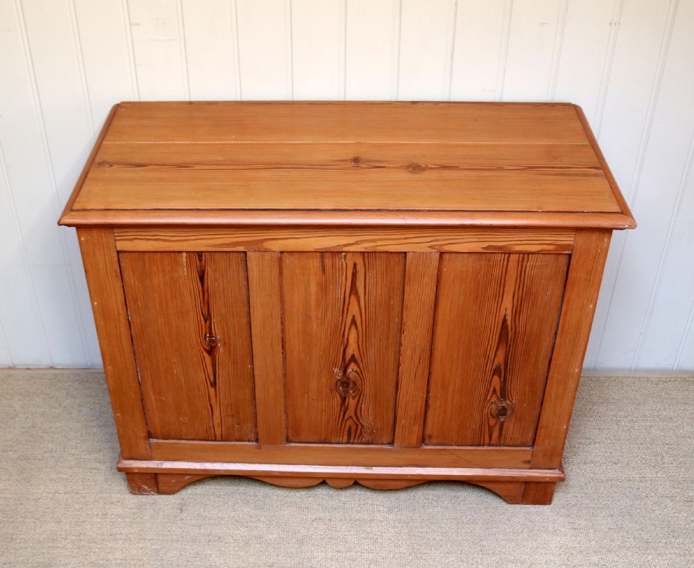 A rectangular warm pine storage box featuring three panelled front sections, a flat hinged top, and a shaped plinth base. View IV