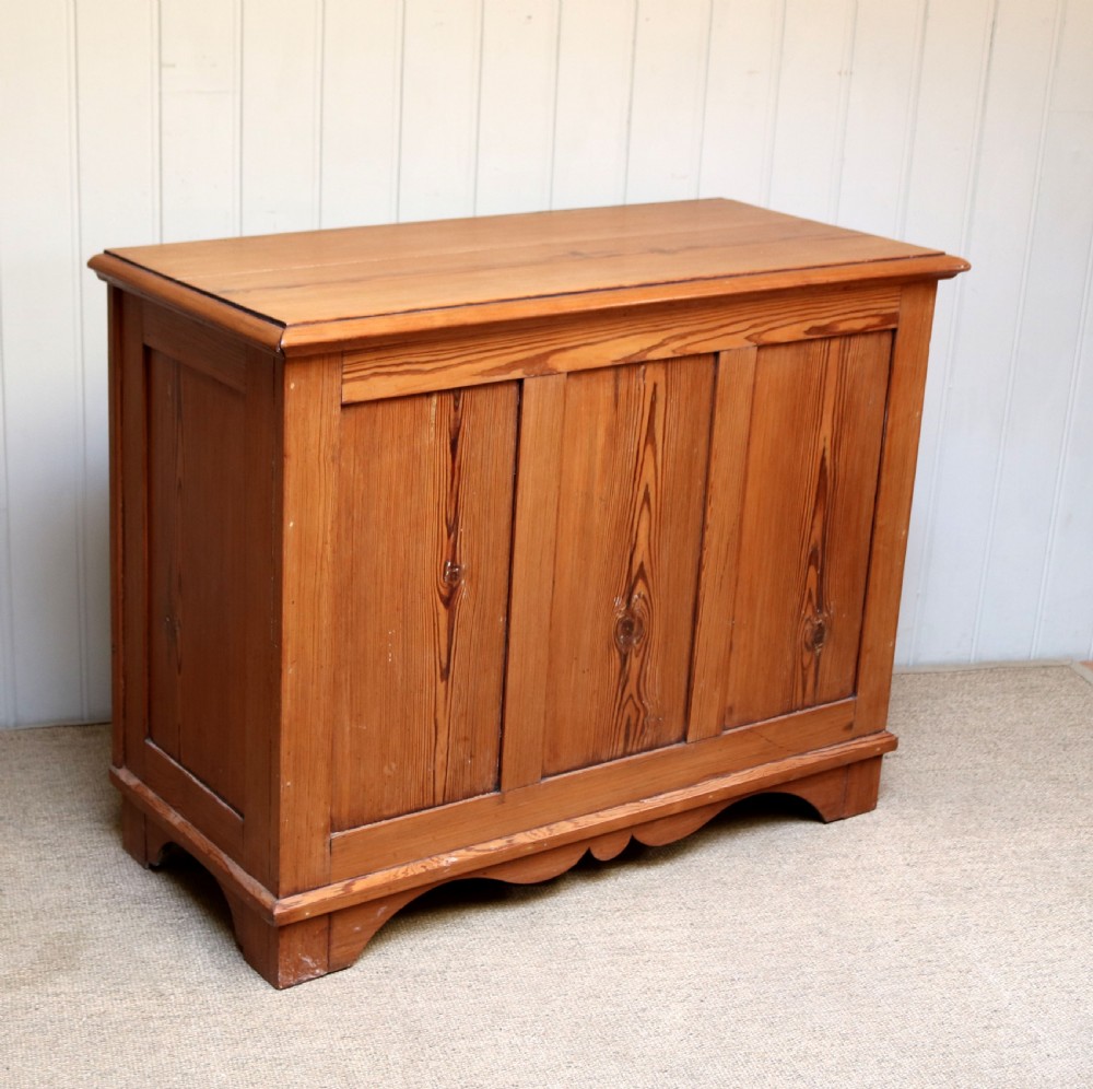 A rectangular warm pine storage box featuring three panelled front sections, a flat hinged top, and a shaped plinth base. View VI