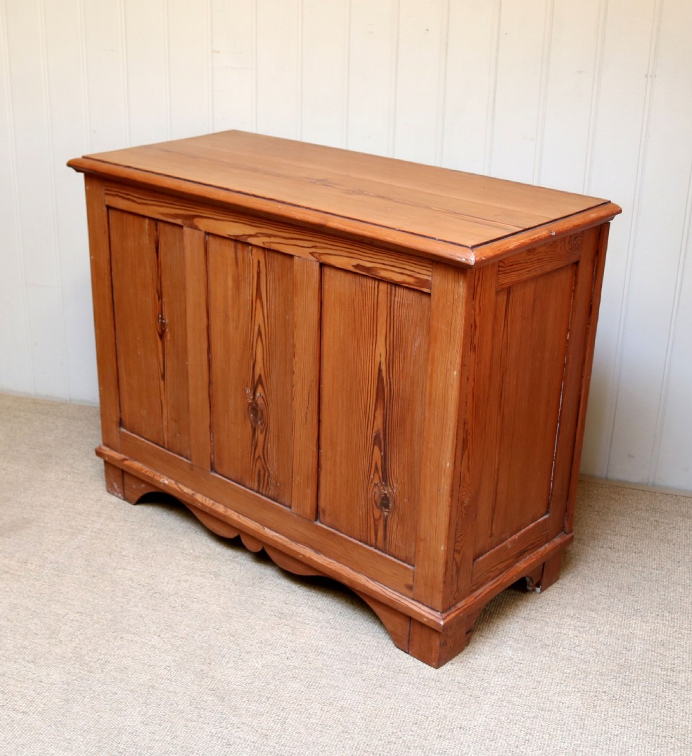 A rectangular warm pine storage box featuring three panelled front sections, a flat hinged top, and a shaped plinth base. View VII