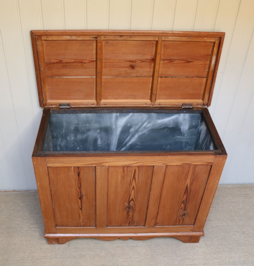 A rectangular warm pine storage box featuring three panelled front sections, a flat hinged top, and a shaped plinth base. View IX