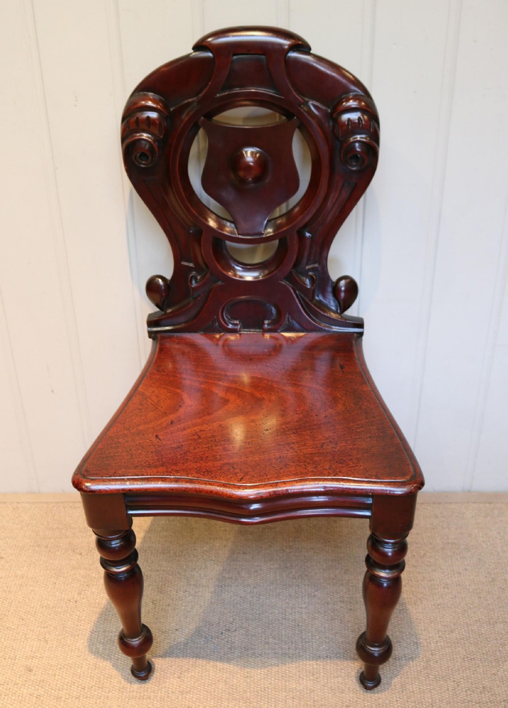 A Mid-Victorian mahogany hall chair featuring an openwork scrollwork backrest, a solid wooden seat, and turned front legs.