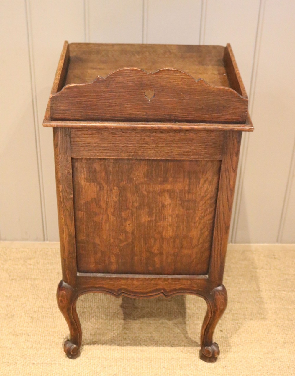 A warm brown solid oak bedside cabinet featuring a heart cut-out gallery, a single drawer, a carved panel door, and cabriole legs. View IX