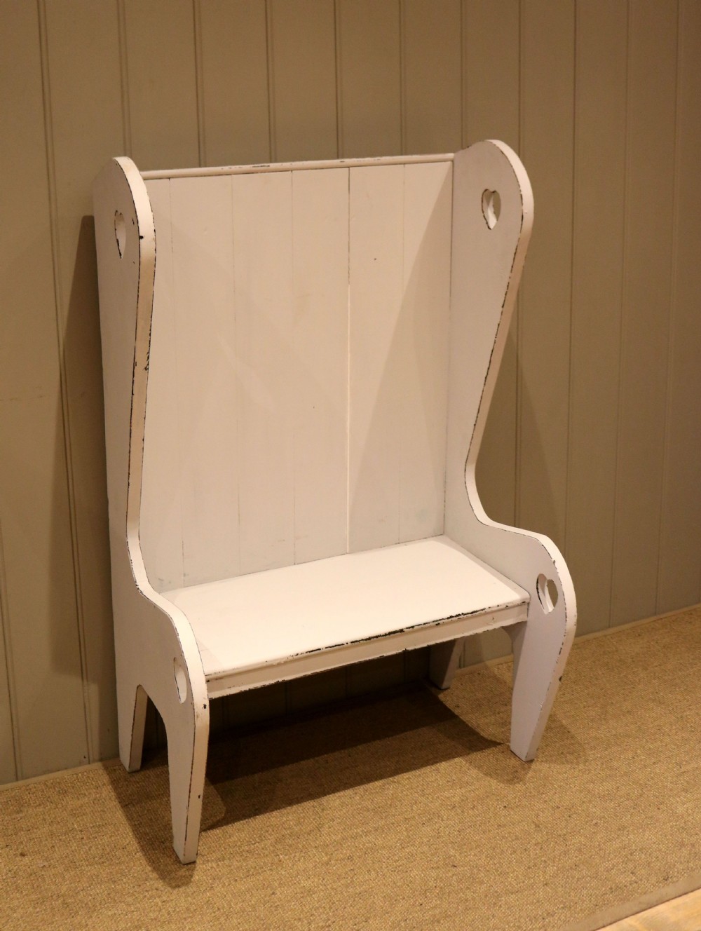 A small off-white painted wooden Arts and Crafts style high-backed settle featuring heart cut-outs on the side panels. View II