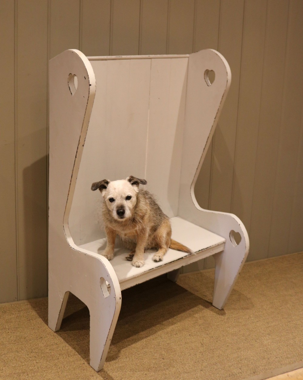 A small off-white painted wooden Arts and Crafts style high-backed settle featuring heart cut-outs on the side panels. View IV