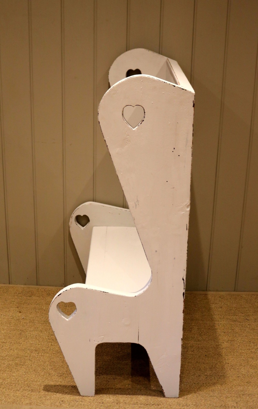 A small off-white painted wooden Arts and Crafts style high-backed settle featuring heart cut-outs on the side panels. View VI