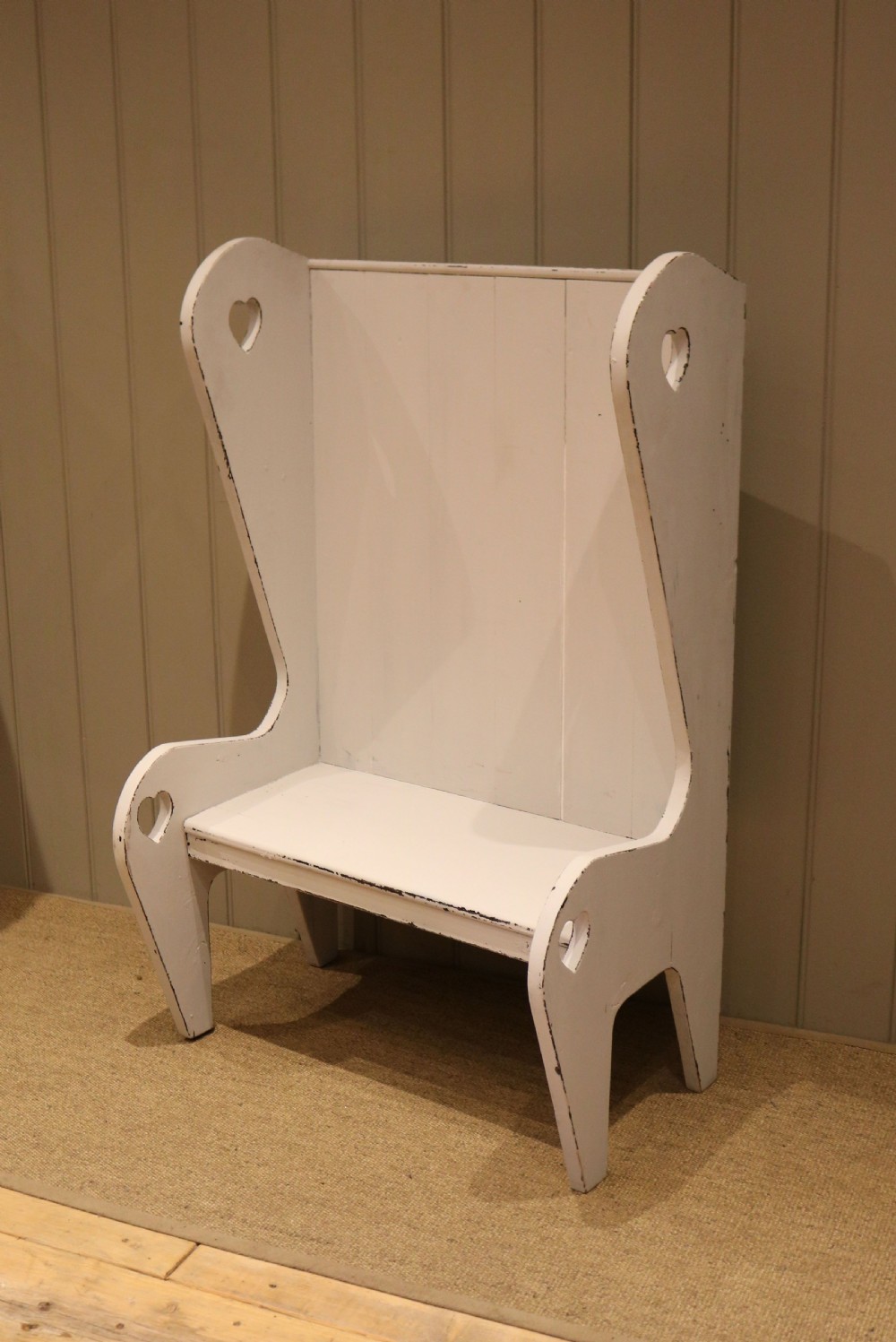 A small off-white painted wooden Arts and Crafts style high-backed settle featuring heart cut-outs on the side panels. View VII