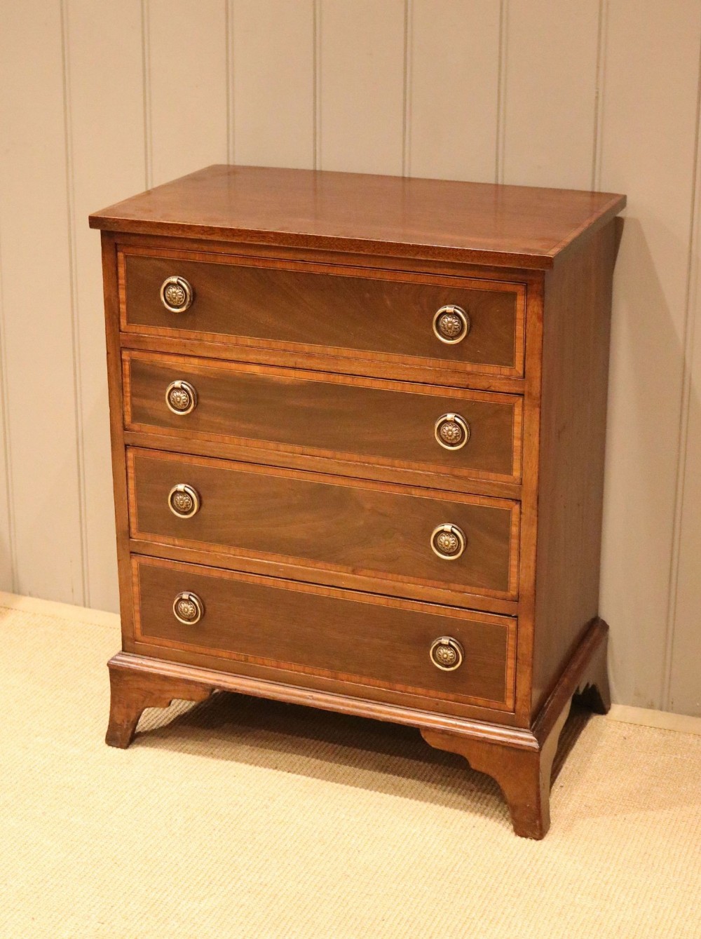 An early 20th-century mahogany chest of drawers featuring four graduated drawers with crossbanded inlay borders, circular brass ring handles, and bracket feet.