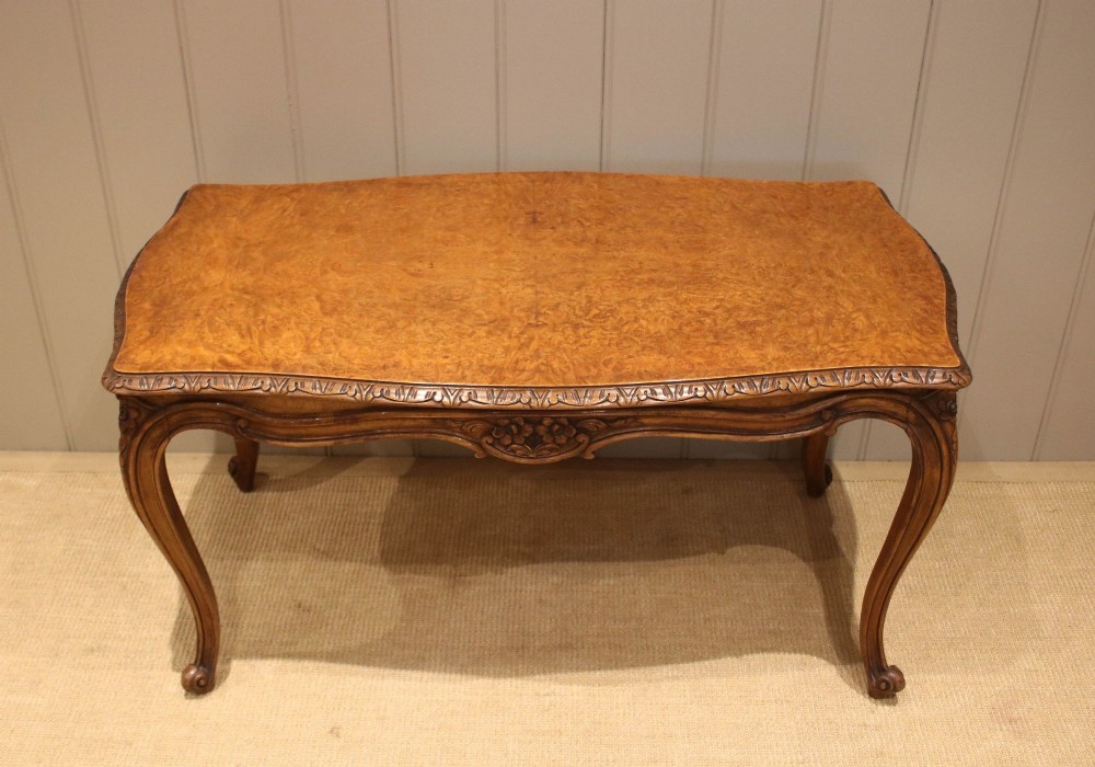 A low rectangular burr walnut coffee table with a serpentine top, hand-carved floral apron, and curved cabriole legs.