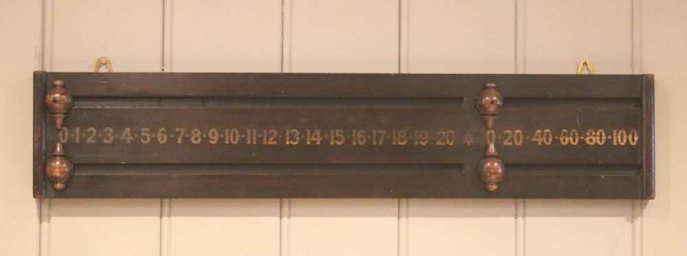 A dark stained wooden billiard scoreboard featuring two sliding turned wooden pointers along horizontal tracks with gold stencilled numbers.