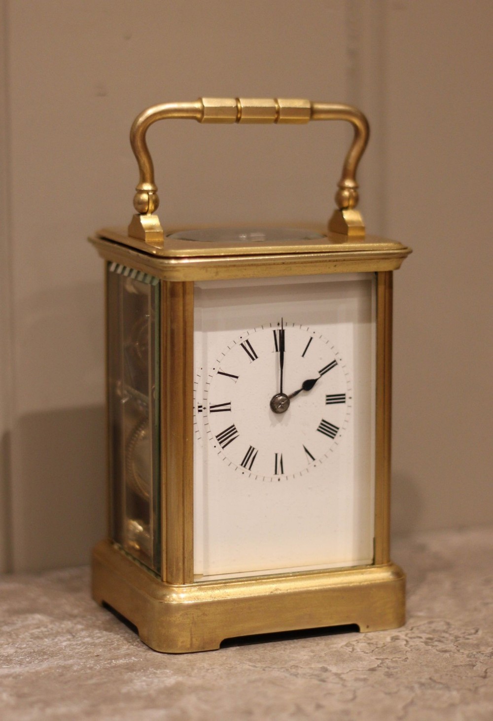 An antique French carriage clock featuring a rectangular gilded brass case with a folding handle, clear glass side panels, and a white enamel dial with black Roman numerals.