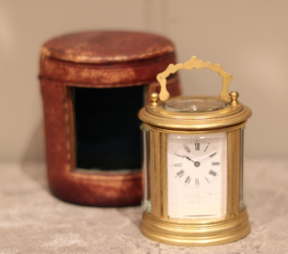 A late 19th-century miniature oval brass carriage clock with a white enamel dial alongside its original fitted leather travel case.