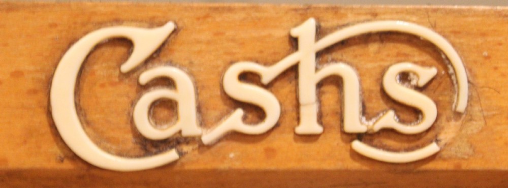 A tall beech wood countertop display case with clear glass panels, interior shelves fitted with brass retainers, and a white Cashs brand logo on the upper frame. View IV