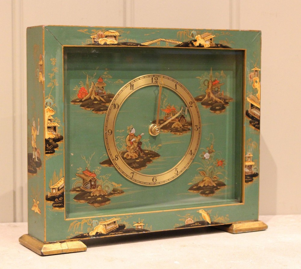 A rectangular green lacquered mantel clock decorated with gilded Chinoiserie scenes and a central brass dial.