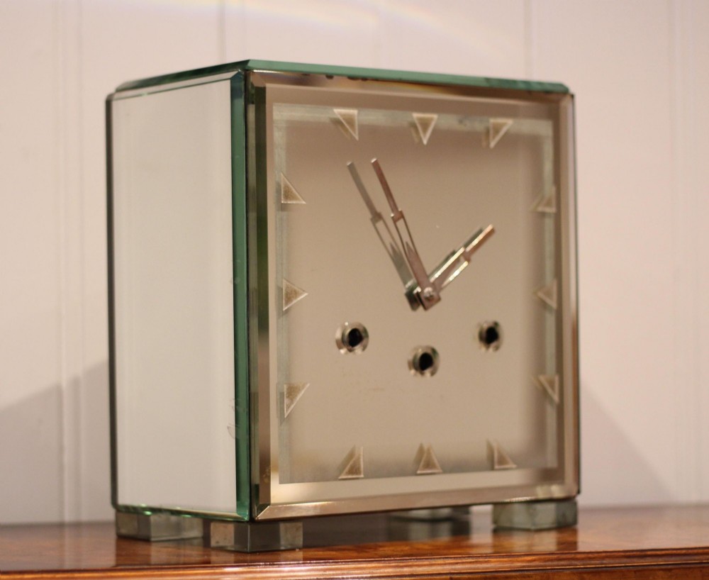 A rectangular Art Deco mantel clock clad in bevelled mirrored glass panels with geometric triangular hour markers and three winding key holes on the dial.