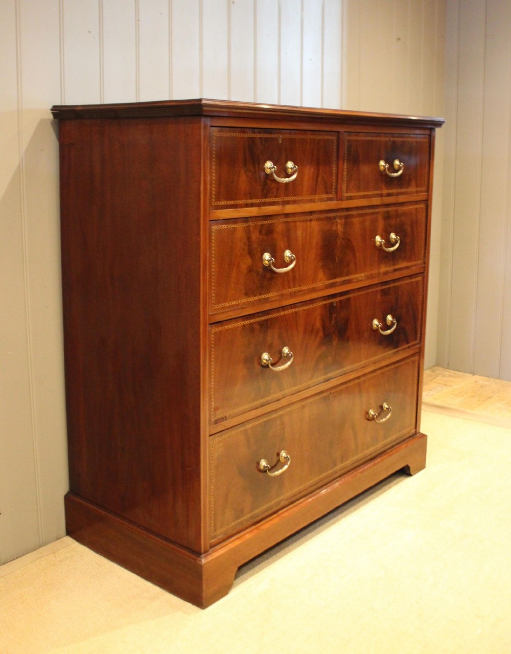 An Edwardian mahogany chest of drawers featuring two short over three long drawers with decorative brass handles and subtle inlaid borders.