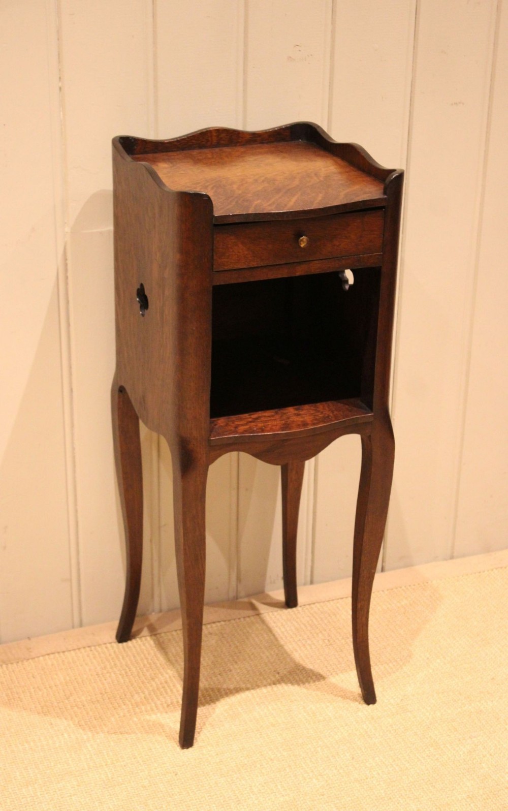 A French dark oak bedside cabinet featuring a shaped tray top, single drawer, open compartment, pierced side cut-outs, and cabriole legs.