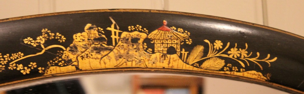 An oval wall mirror featuring a black lacquered wood frame decorated with intricate gold Chinoiserie landscapes, figures, and geometric patterns. View IX