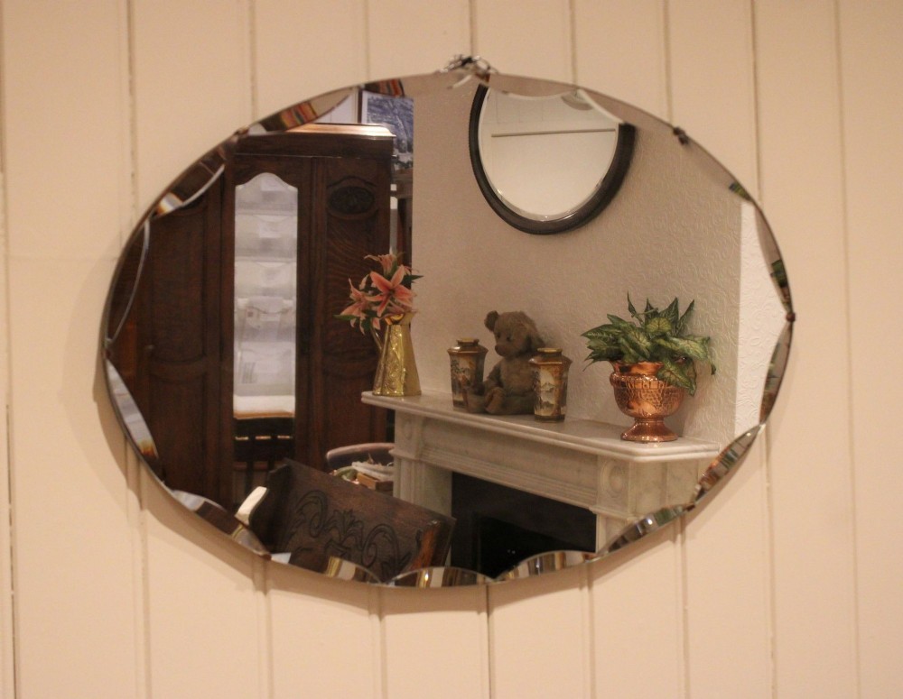 An oval frameless wall mirror featuring a decorative scalloped bevelled glass edge.