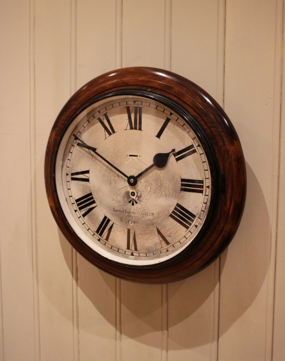 A circular 1940s wall clock featuring a turned beech wood bezel surround and an aged dial with black Roman numerals. View VI