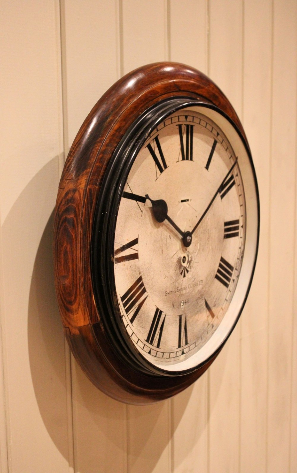 A circular 1940s wall clock featuring a turned beech wood bezel surround and an aged dial with black Roman numerals. View IX