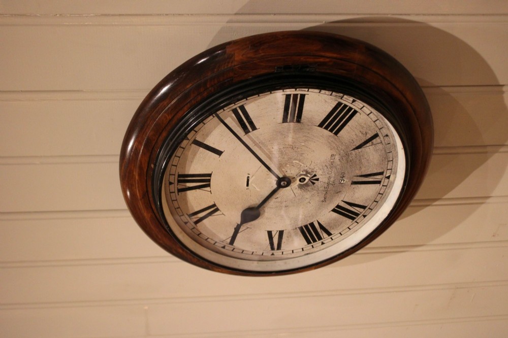 A circular 1940s wall clock featuring a turned beech wood bezel surround and an aged dial with black Roman numerals. View X