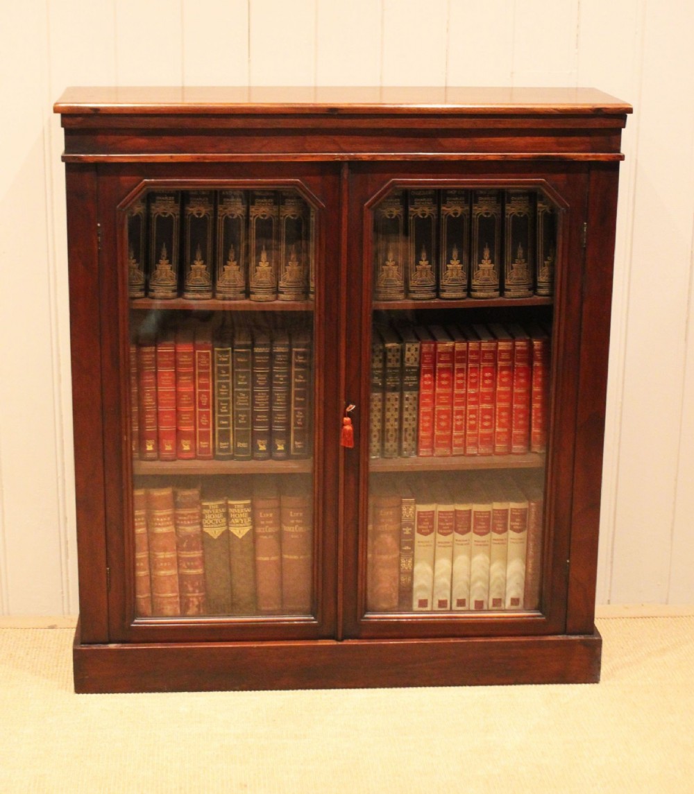 A late nineteenth-century dark mahogany bookcase with two glazed doors and interior shelves containing rows of books.