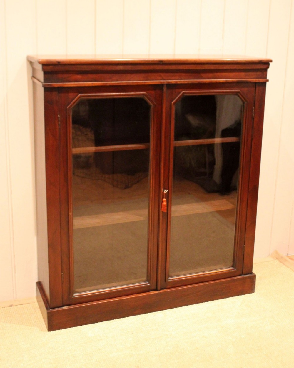 A late nineteenth-century dark mahogany bookcase with two glazed doors and interior shelves containing rows of books. View II