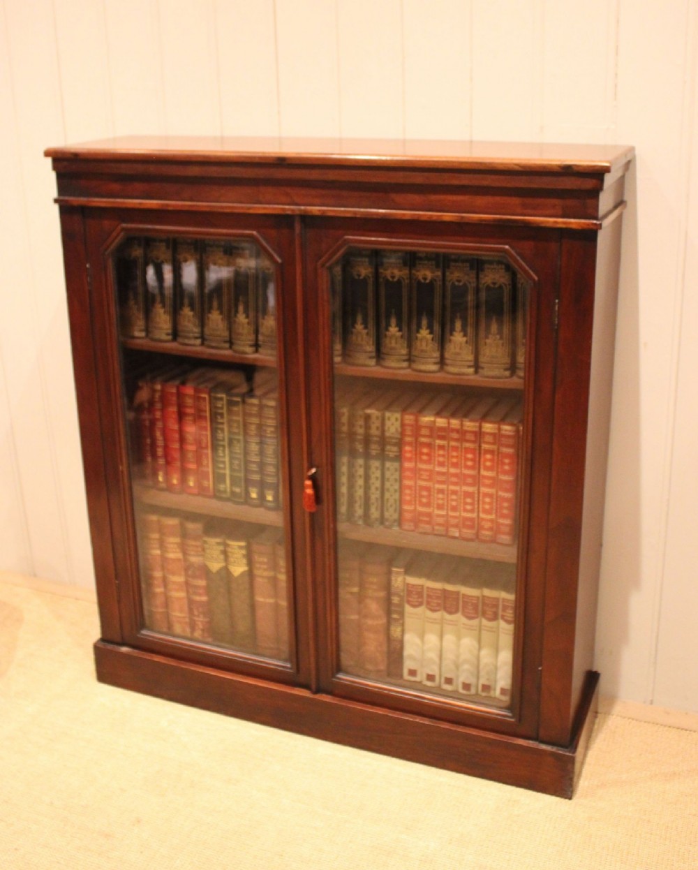 A late nineteenth-century dark mahogany bookcase with two glazed doors and interior shelves containing rows of books. View III