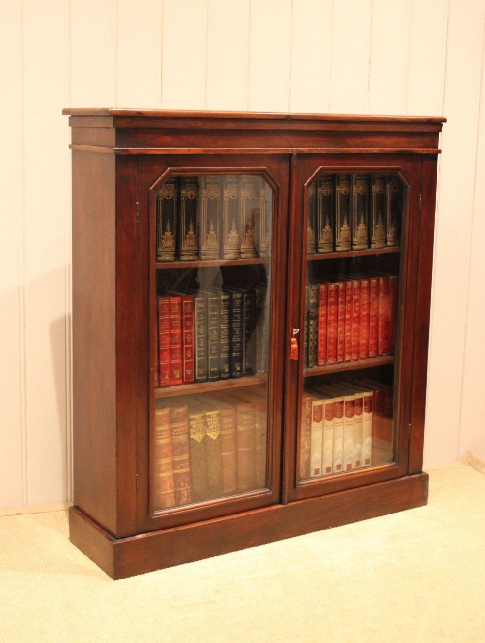 A late nineteenth-century dark mahogany bookcase with two glazed doors and interior shelves containing rows of books. View V