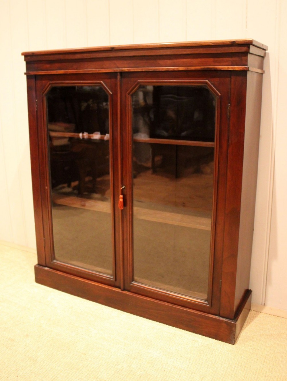 A late nineteenth-century dark mahogany bookcase with two glazed doors and interior shelves containing rows of books. View X
