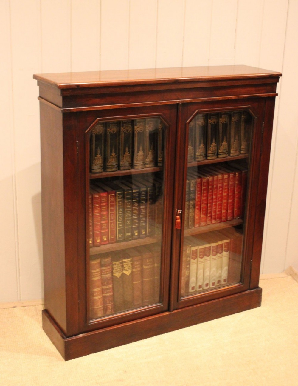 A late nineteenth-century dark mahogany bookcase with two glazed doors and interior shelves containing rows of books. View XI