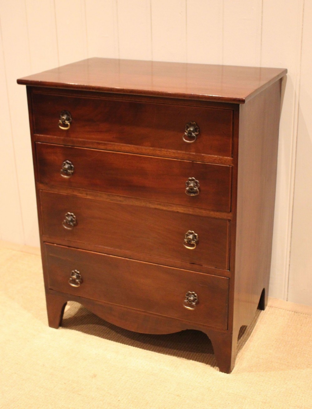 An Edwardian mahogany chest of drawers with four graduated drawers, circular brass handles, and a shaped apron base.