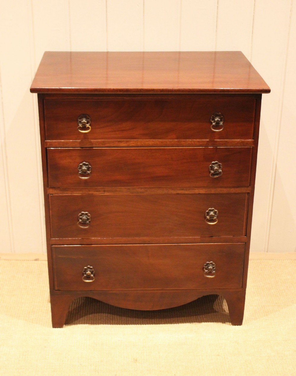 An Edwardian mahogany chest of drawers with four graduated drawers, circular brass handles, and a shaped apron base. View II