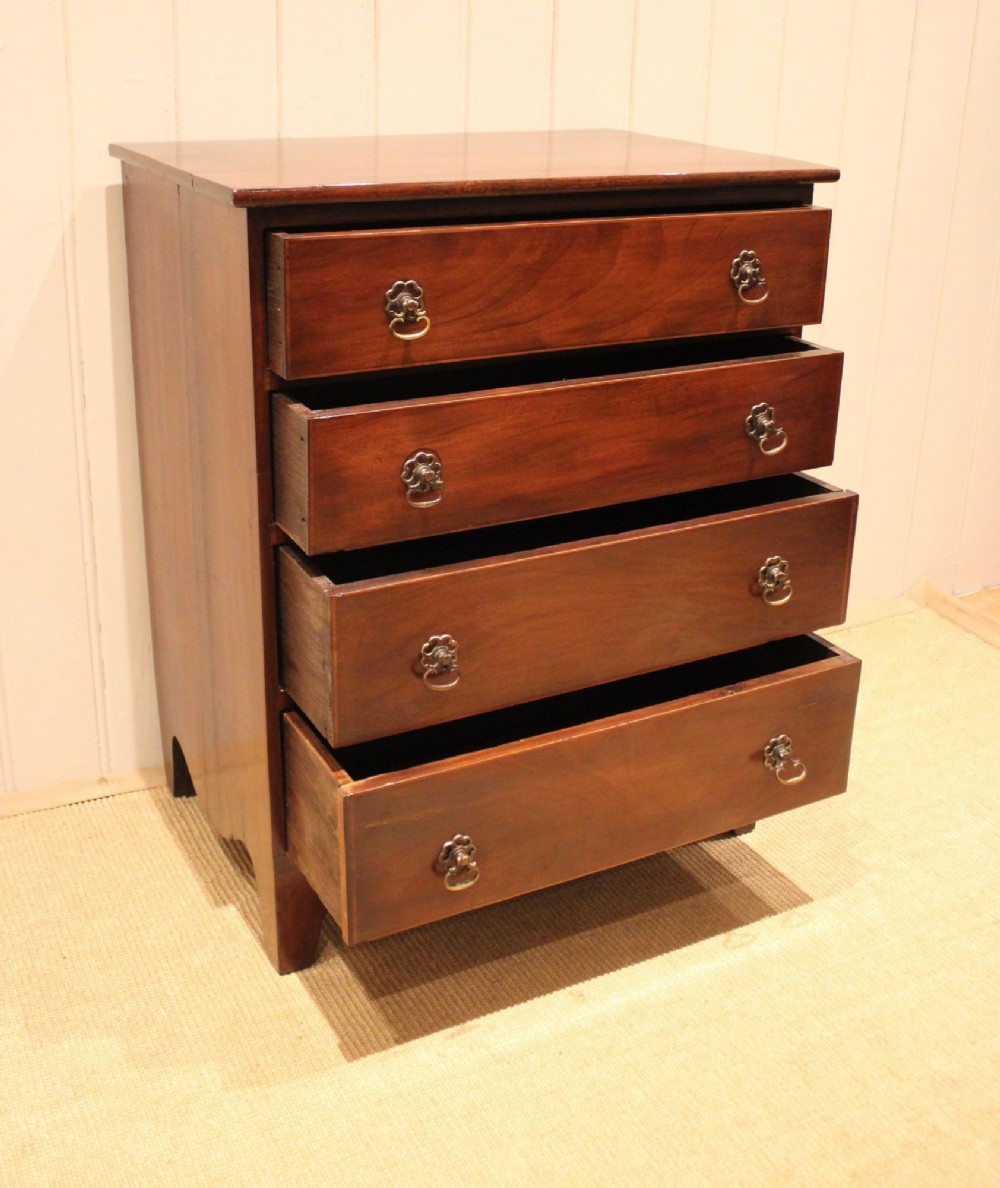 An Edwardian mahogany chest of drawers with four graduated drawers, circular brass handles, and a shaped apron base. View IV