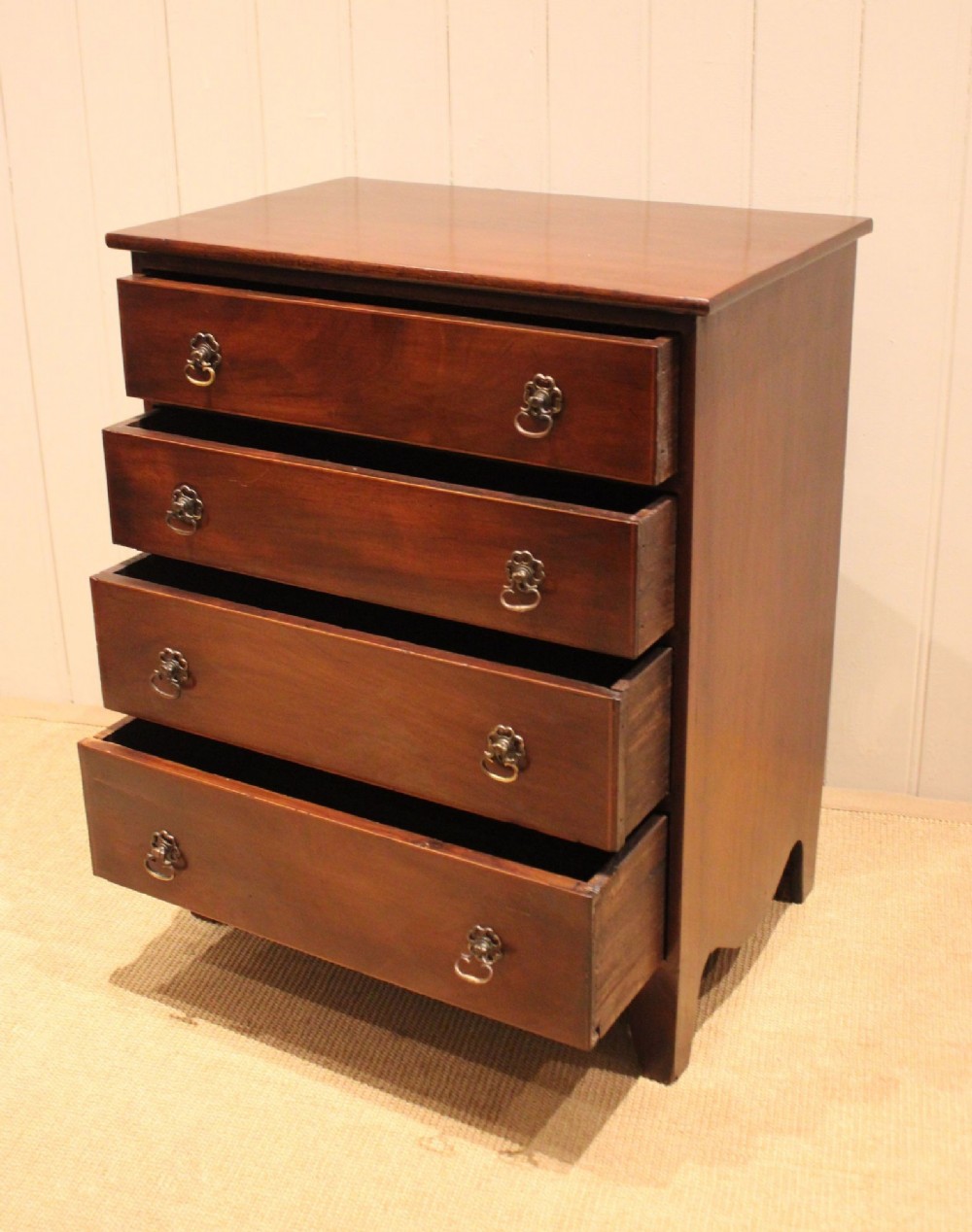 An Edwardian mahogany chest of drawers with four graduated drawers, circular brass handles, and a shaped apron base. View V