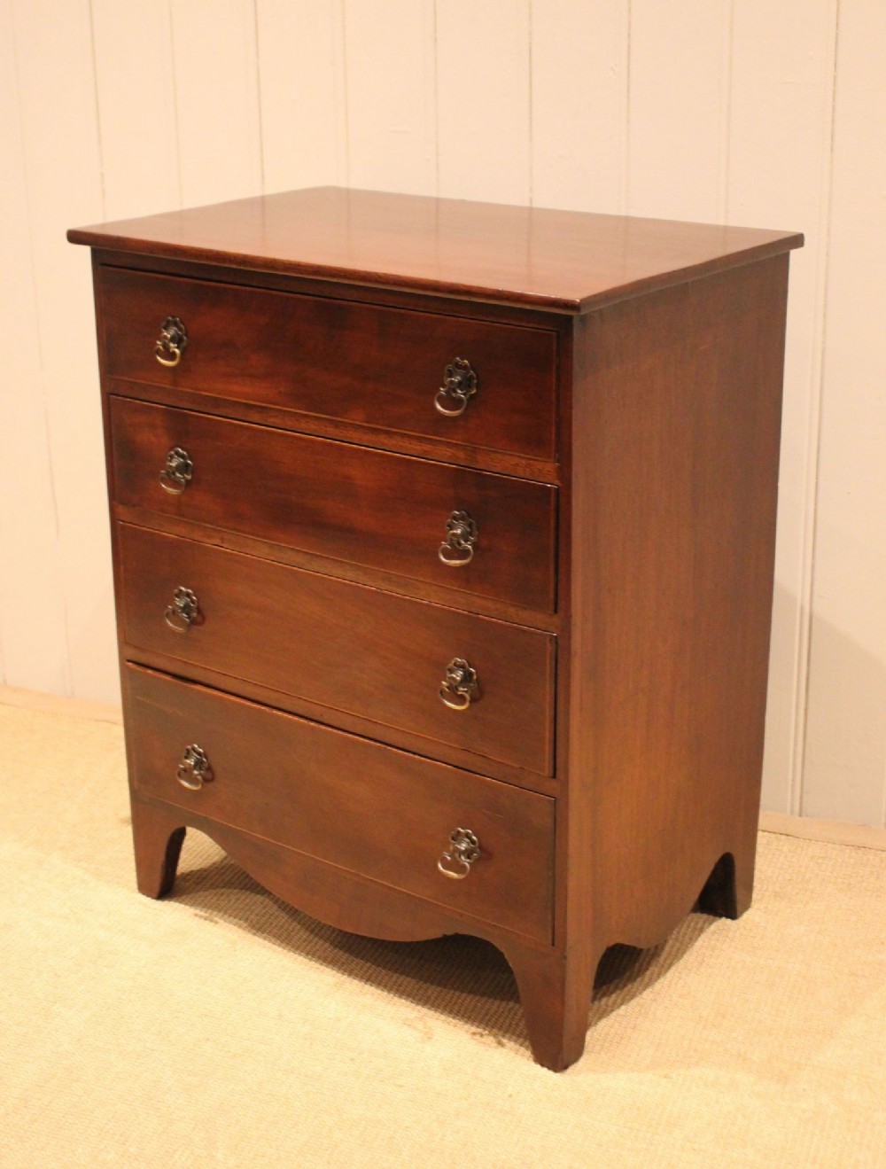 An Edwardian mahogany chest of drawers with four graduated drawers, circular brass handles, and a shaped apron base. View VII