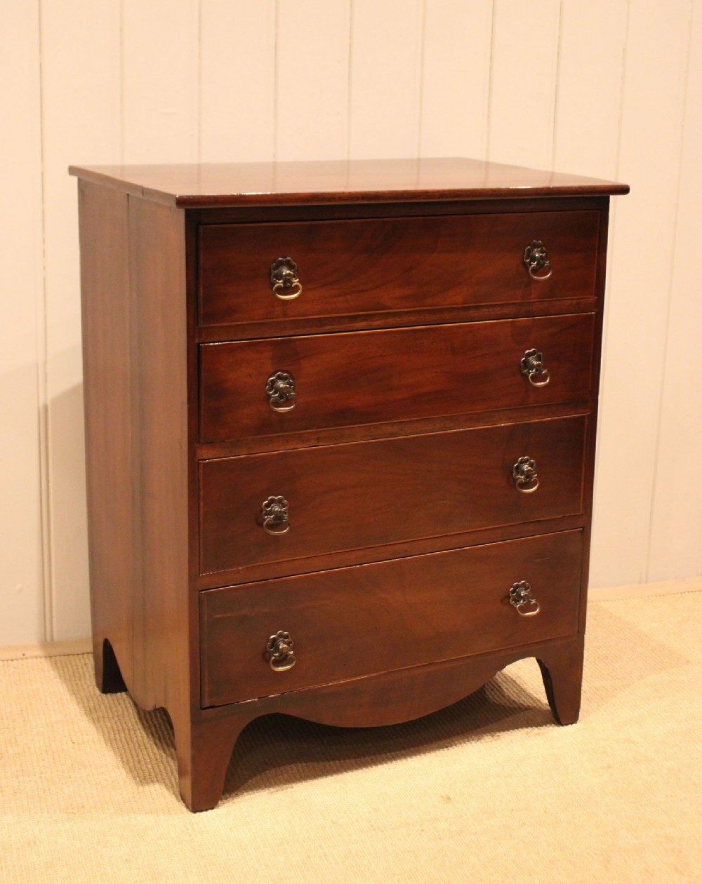 An Edwardian mahogany chest of drawers with four graduated drawers, circular brass handles, and a shaped apron base. View VIII