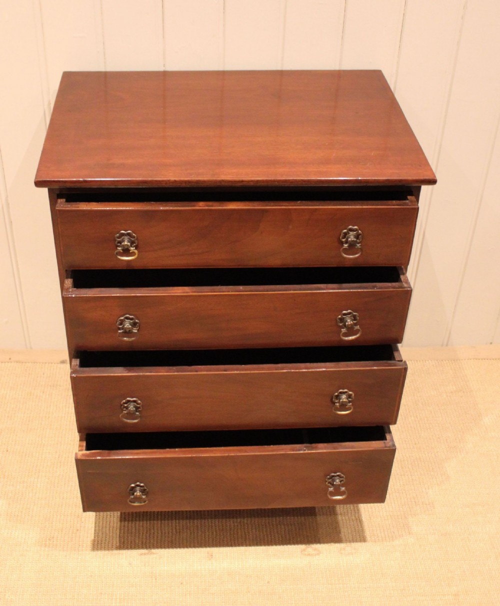 An Edwardian mahogany chest of drawers with four graduated drawers, circular brass handles, and a shaped apron base. View X