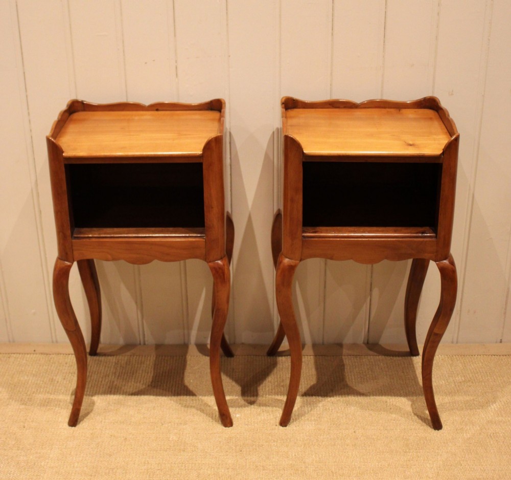 A pair of warm brown cherry wood bedside cabinets featuring open shelf compartments, scalloped top galleries, and slender cabriole legs.