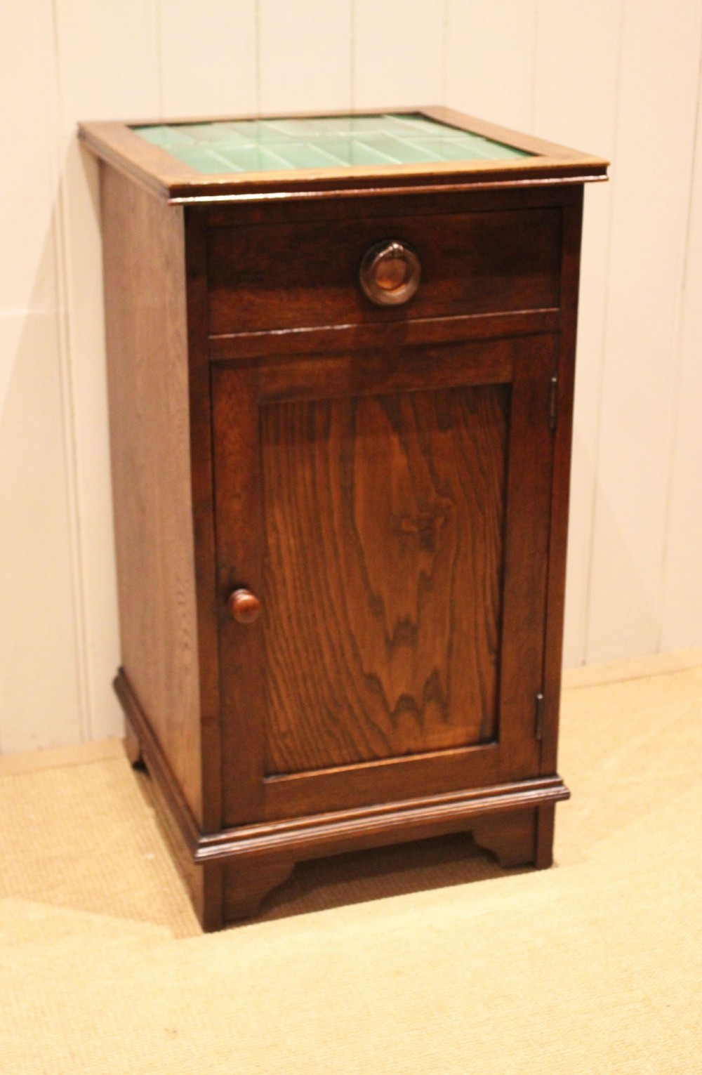 An Arts and Crafts oak cabinet featuring a recessed green glazed tile top, a single drawer with a round ring pull, and a lower panelled cupboard door. View V