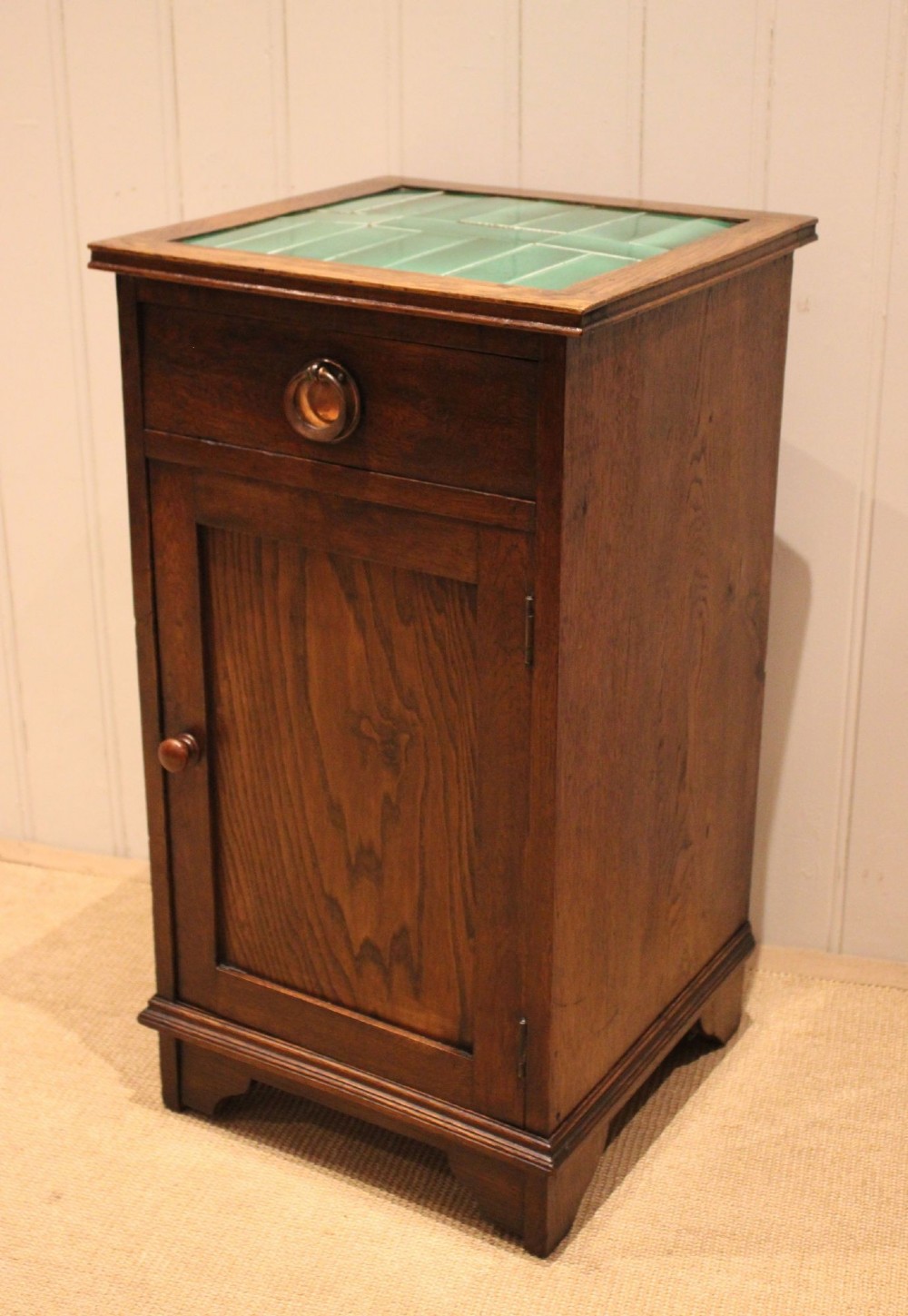 An Arts and Crafts oak cabinet featuring a recessed green glazed tile top, a single drawer with a round ring pull, and a lower panelled cupboard door. View IX
