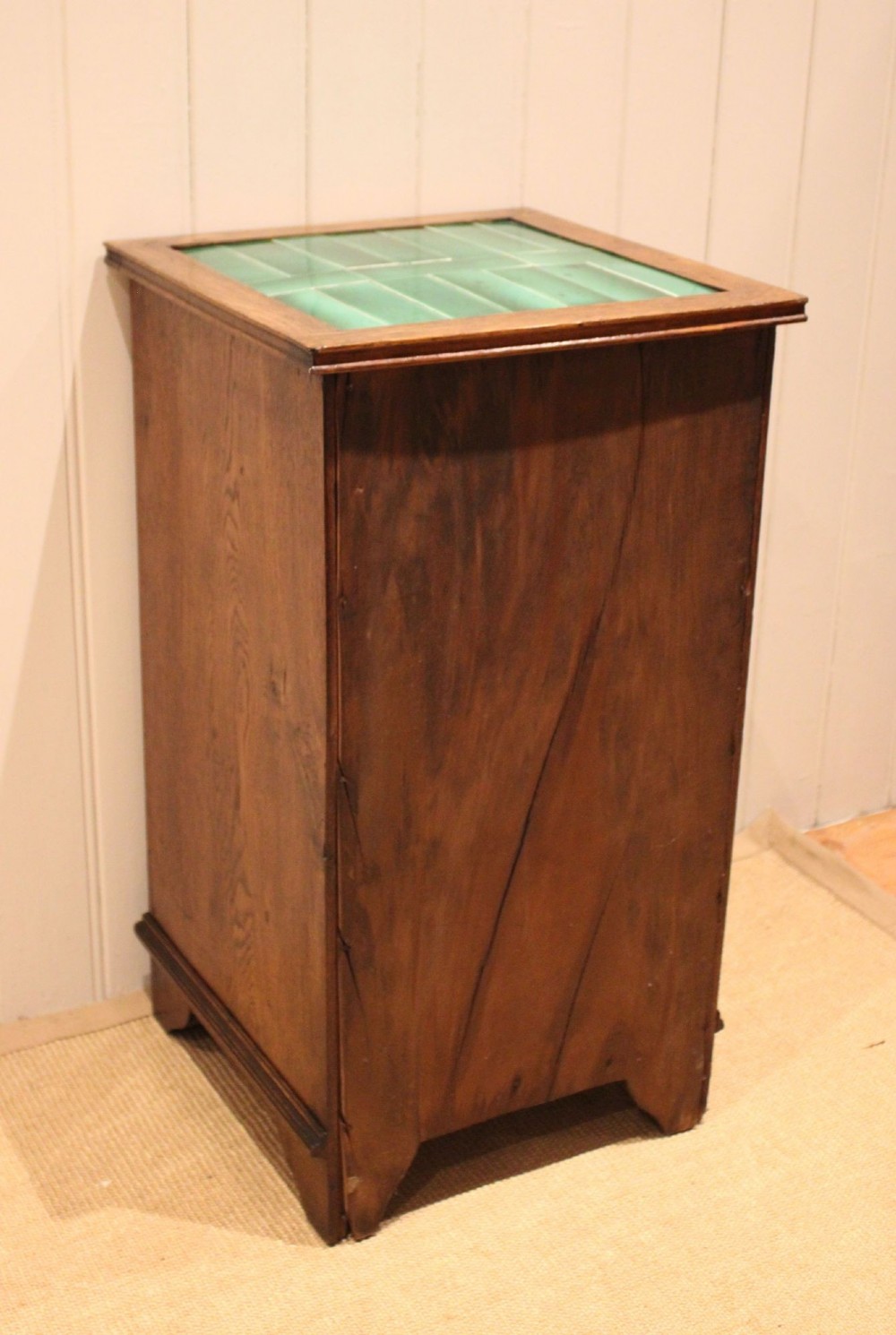 An Arts and Crafts oak cabinet featuring a recessed green glazed tile top, a single drawer with a round ring pull, and a lower panelled cupboard door. View XII