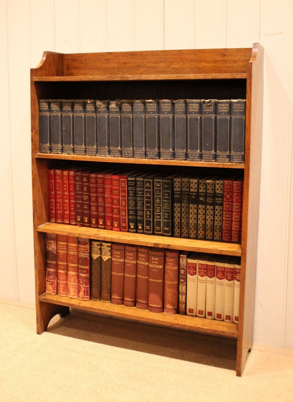 A golden oak open bookcase featuring four tiered shelves filled with antique books and a shaped top upstand gallery.