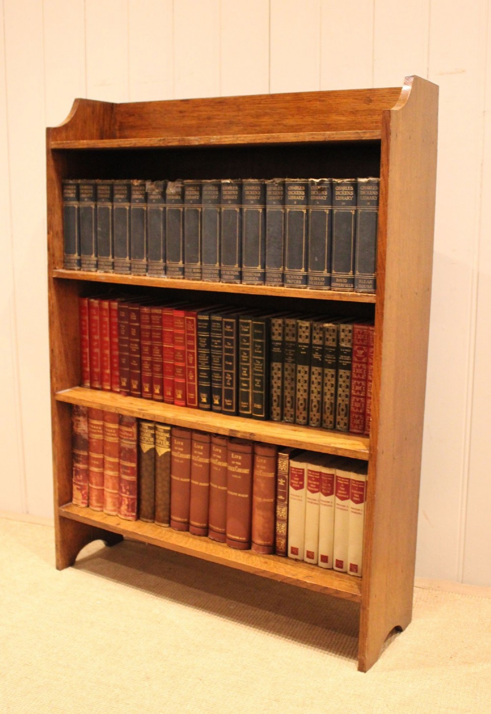 A golden oak open bookcase featuring four tiered shelves filled with antique books and a shaped top upstand gallery. View III