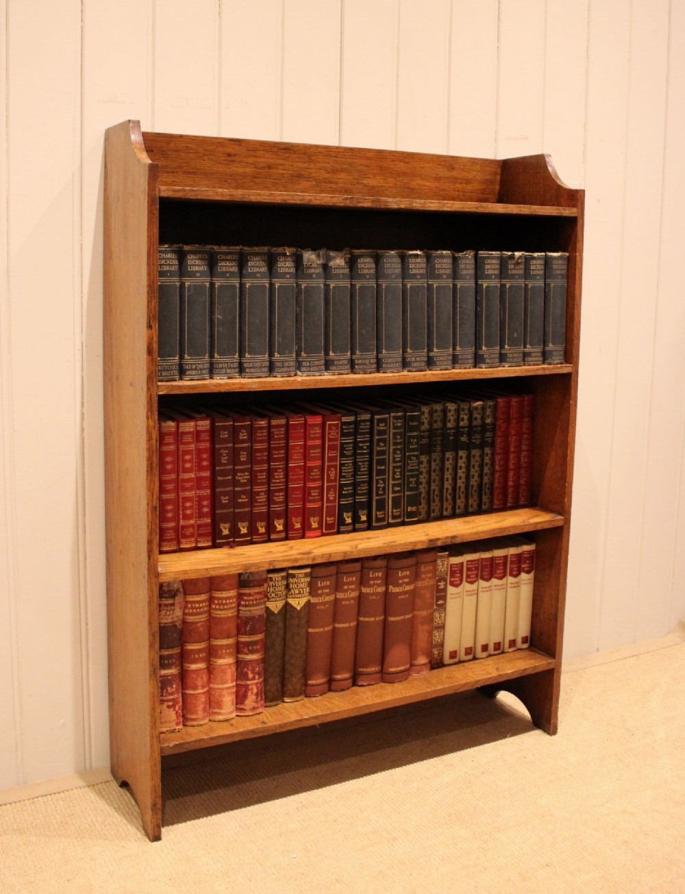 A golden oak open bookcase featuring four tiered shelves filled with antique books and a shaped top upstand gallery. View V
