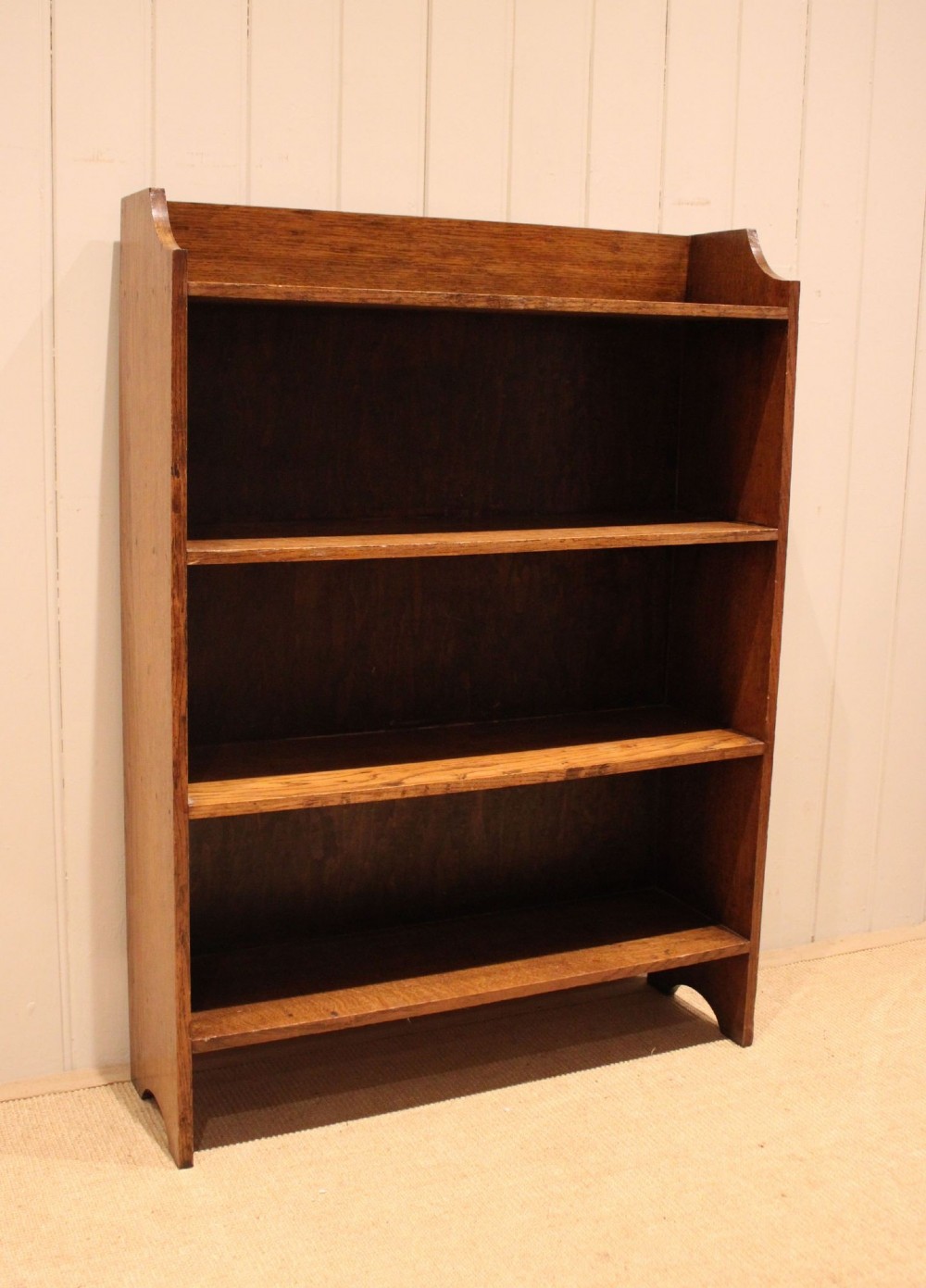 A golden oak open bookcase featuring four tiered shelves filled with antique books and a shaped top upstand gallery. View X