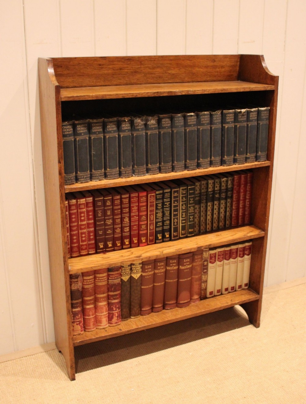 A golden oak open bookcase featuring four tiered shelves filled with antique books and a shaped top upstand gallery. View XI
