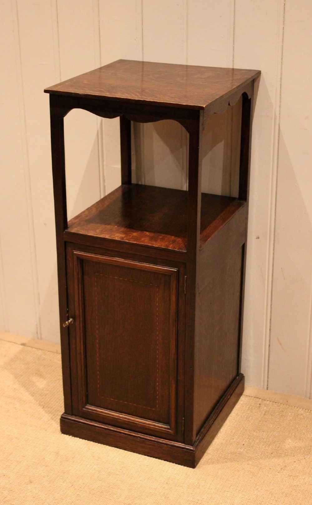 A dark oak Edwardian bedside cabinet with an open upper shelf, shaped apron, and a panelled single door below.