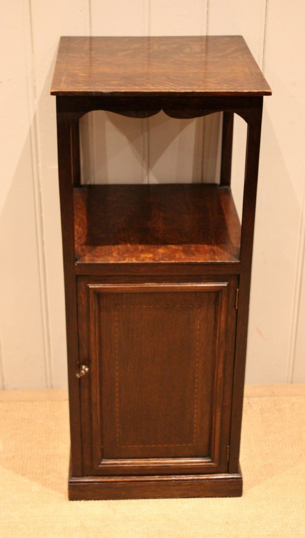 A dark oak Edwardian bedside cabinet with an open upper shelf, shaped apron, and a panelled single door below. View II