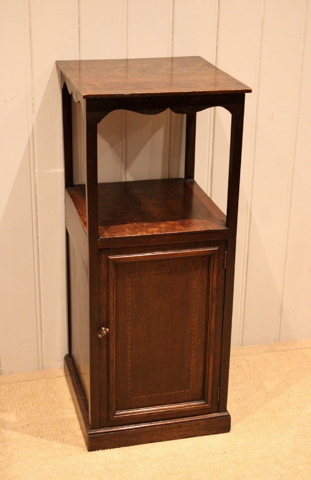 A dark oak Edwardian bedside cabinet with an open upper shelf, shaped apron, and a panelled single door below. View III